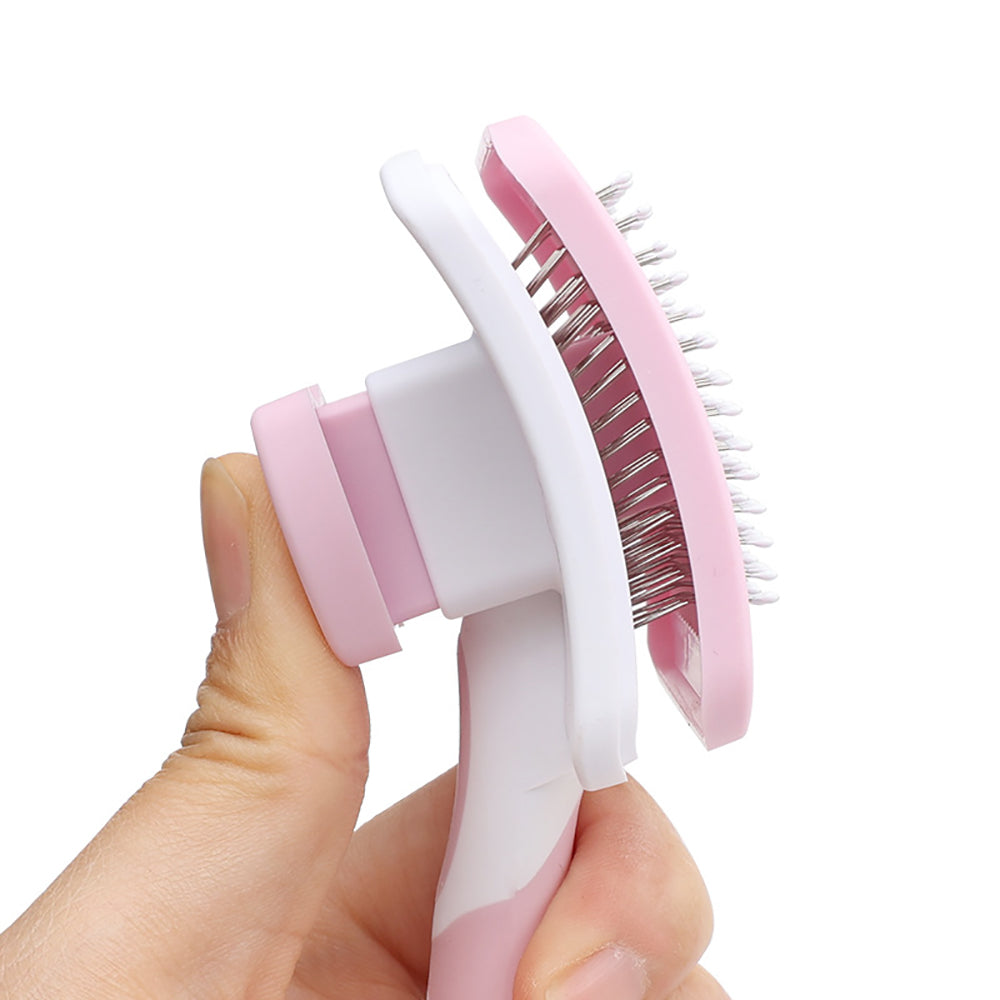 Hand holding pink and white pet grooming brush with stainless steel bristles